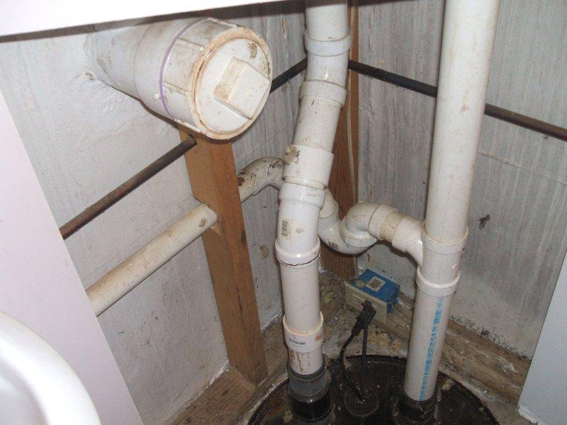 Responded to sewage lift pump issue where existing sump pump required replacement due to sump basin being positioned lower than the drain field elevation. Assessed plumbing assembly in confined utility space with multiple white PVC discharge lines and existing black pump unit with blue control sensor. Replaced failed sump pump system to restore proper sewage lifting capability and ensure adequate discharge pressure to overcome elevation differential to drain field.