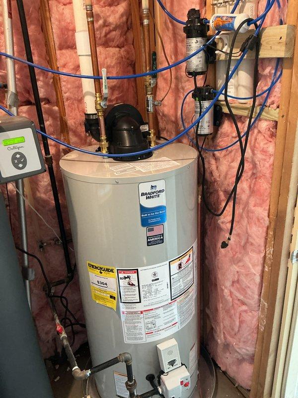 Installed a 50-gallon Bradford White power draft water heater in an unfinished utility space with exposed wall studs. Connected hot and cold water copper lines with brass fittings, integrated existing blue PEX tubing lines, and mounted circulation pump on top of unit. Installed pressure relief valve, shut-off valves, and completed all electrical connections per manufacturer specifications.