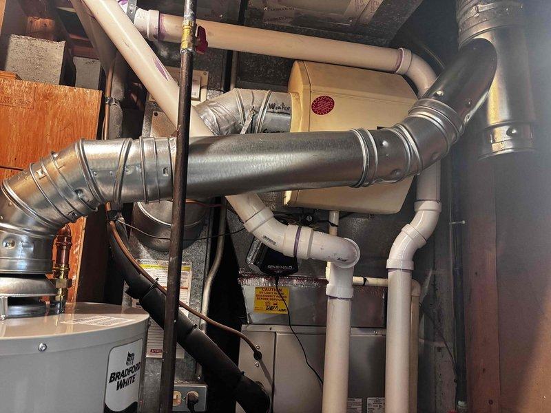 Completed installation of Bradford White natural draft 40-gallon water heater in residential basement utility area. Removed existing unit and installed new slim-profile model with proper copper supply line connections, brass shut-off valves, and metallic vent ductwork. Connected black PVC drain piping to code-compliant relief valve assembly, mounted unit on elevated platform, and verified all plumbing connections, gas lines, and ventilation system for proper operation and safety compliance.