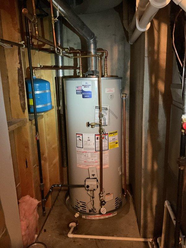 Completed installation of a 75-gallon natural gas water heater with 6-year warranty in residential utility space. Installation included proper venting with black flue pipe, connection of copper supply lines with brass fittings, installation of blue expansion tank with secure wall mounting, and installation of restricting valve for code compliance. All work completed to manufacturer specifications with proper clearances maintained in confined basement mechanical room setting.