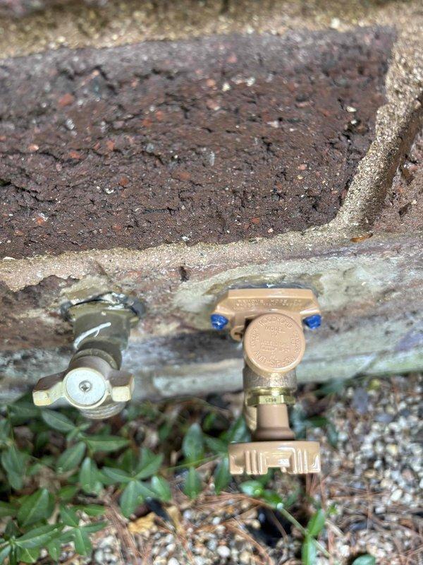 Responded to follow-up service call for persistent leak at exterior hose bib installation. Upon arrival, inspected three brass hose bibs mounted on exterior brick wall and associated plumbing components beneath concrete foundation. Located source of ongoing leak at pressure regulator valve assembly with blue adjustment screws. Tightened connections at regulator body and verified proper seating of valve components. Tested all three hose bib fixtures under pressure to ensure complete water-tight seal. Confirmed leak resolution and proper operation of all exterior water connections.