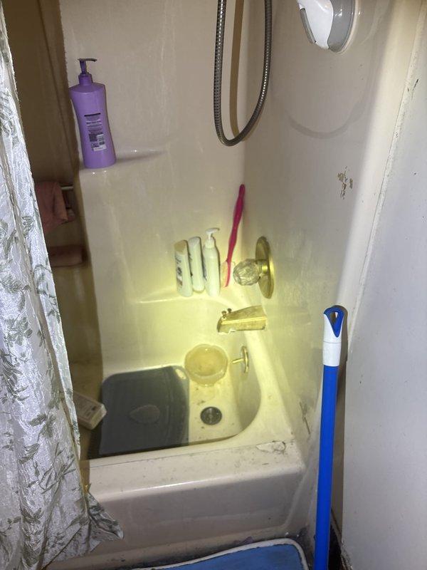 Responded to plumbing leak complaint with water infiltrating kitchen ceiling light fixture from bathroom above and additional water accumulation on kitchen floor. Conducted thorough inspection of bathroom fixtures, including bathtub, shower assembly, toilet, and associated plumbing connections in forty-year-old condo unit. Documented conditions of bathroom plumbing fixtures and surrounding areas with photographic evidence showing aged fiberglass shower surround, chrome fixtures, toilet installation, and deteriorated wall conditions that may contribute to moisture intrusion. Due to customer's inability to access basement area, leak source determination was limited to upper-level bathroom inspection; recommended follow-up investigation of basement plumbing lines and drainage systems to identify definitive source of water infiltration affecting kitchen below.