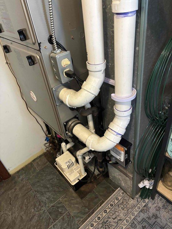 Successfully completed add-on air conditioning system installation. Installed new outdoor condensing unit with proper refrigerant charge and compressor oil levels verified and documented. Indoor air handler cabinet installed with secure panel latches and proper mounting. Configured complete condensate drainage system using white PVC piping with multiple elbows and vertical runs, all secured with proper mounting brackets. Installed condensate pump with associated tubing and flexible connections to ensure reliable water removal. Ran refrigerant line set connecting outdoor and indoor units, properly insulated and secured along wall pathway. Installed electrical control box with appropriate conduit and power connections. All components tested and verified operational.