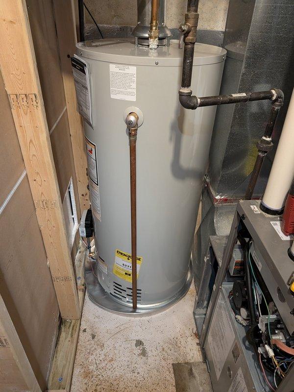 Completed installation of 40-gallon natural gas water heater with non-damper vent configuration in residential utility room. Unit was positioned between existing wall framing and concrete block structure, with all copper supply lines, gas connections, and pressure relief valve properly installed and secured. Blue expansion tank mounted to wooden framing above unit with appropriate copper piping connections, shutoff valves installed on both hot and cold water lines, and all connections tested for proper operation and leak-free performance.