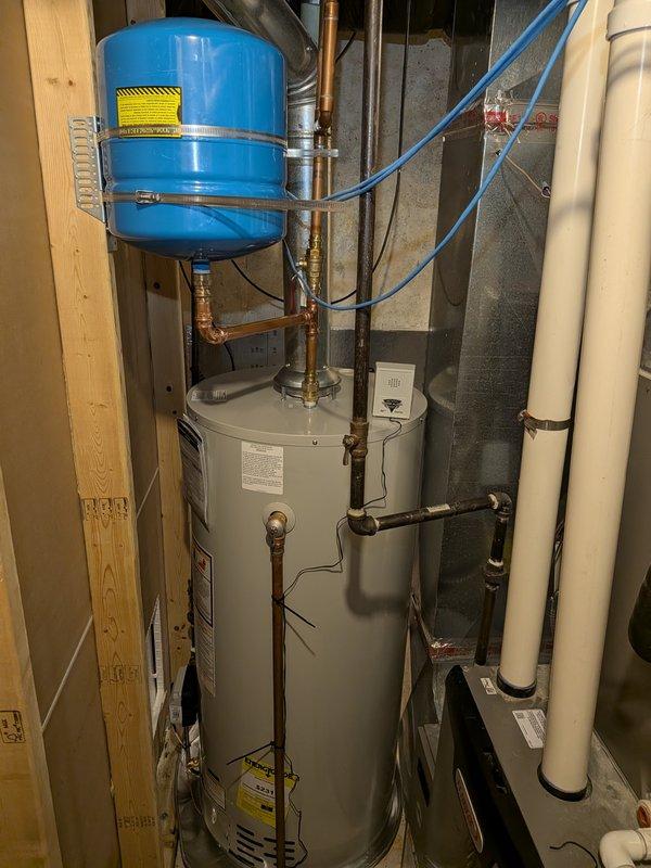 Completed installation of 40-gallon natural gas water heater with non-damper vent configuration in residential utility room. Unit was positioned between existing wall framing and concrete block structure, with all copper supply lines, gas connections, and pressure relief valve properly installed and secured. Blue expansion tank mounted to wooden framing above unit with appropriate copper piping connections, shutoff valves installed on both hot and cold water lines, and all connections tested for proper operation and leak-free performance.