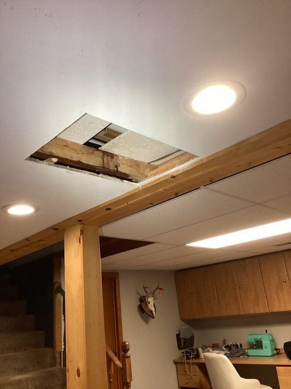 Responded to water leak in basement. Upon investigation, discovered active leak originating from plumbing penetration through ceiling cavity near HVAC ductwork. Removed section of ceiling drywall to access leak source and assess damage to surrounding structural members. Identified moisture infiltration affecting wooden joists and ceiling materials. Documented conditions with photographs showing exposed ceiling cavity, stained framing members, and proximity to galvanized ductwork and plumbing components. Provided assessment and recommendations for necessary repairs to resolve leak and restore affected ceiling area.
