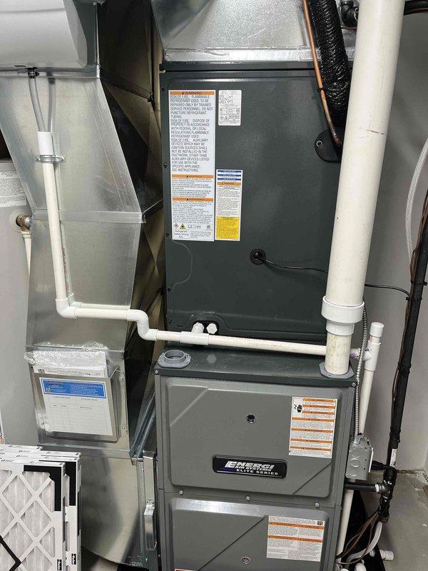 Completed full HVAC system installation including Bryant furnace and outdoor condensing unit. Furnace installed in basement utility area with proper PVC venting, ductwork connections, and air filtration system. Outdoor AC unit positioned on concrete pad adjacent to building exterior with appropriate clearances and refrigerant line connections established between indoor and outdoor components.