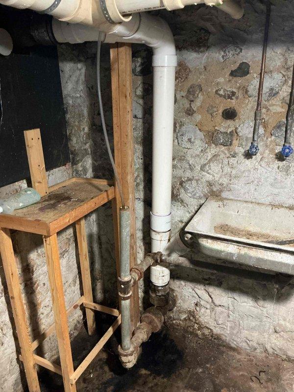 Completed drain repair in basement utility area involving replacement of severely corroded metal drainage piping. Removed deteriorated sections exhibiting extensive rust and corrosion, then installed new white PVC drainage pipes with proper rubber couplings to ensure watertight connections. Work included vertical and horizontal pipe runs, integration with existing plumbing system, and verification of proper drainage flow upon completion.