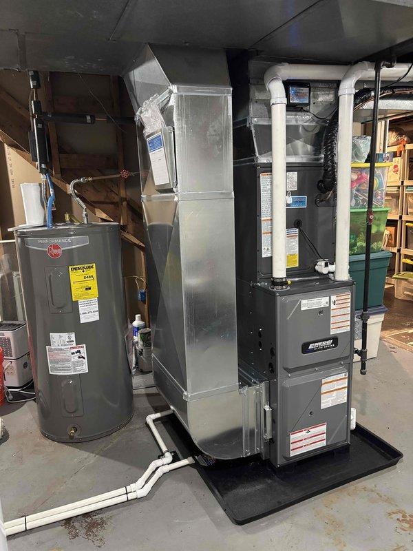 Completed full installation of residential furnace and air conditioning system in basement mechanical room. New HVAC system includes modern air handler unit with proper PVC condensate drainage lines, ventilation piping, and black drain pan installation on concrete floor. All equipment properly connected to existing ductwork, electrical service, and plumbing connections with appropriate safety labels and manufacturer specifications verified. System tested and operational upon completion.