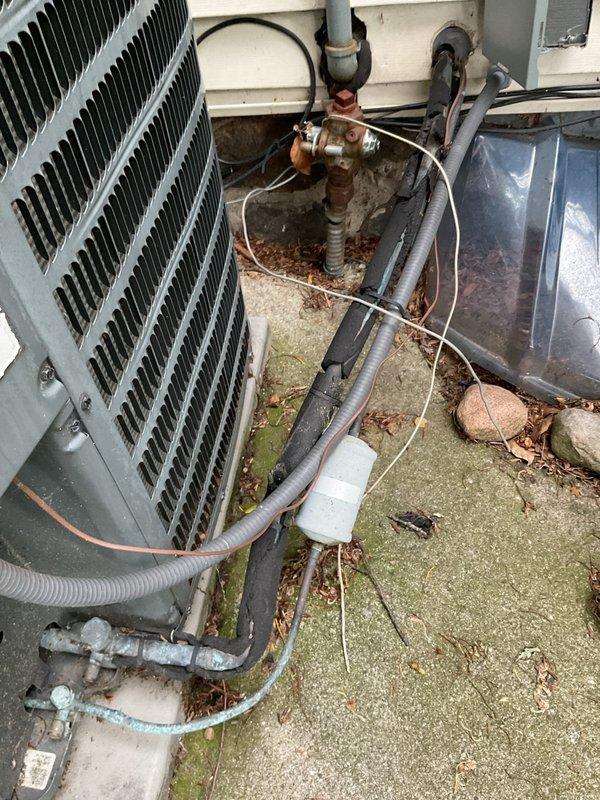 Completed annual cooling maintenance on 17-year-old residential air conditioning system. Performed comprehensive tune-up including inspection of outdoor condenser unit, refrigerant line connections, and associated mechanical components. System found to be in good operating condition with all components functioning within normal parameters. Documented equipment condition with photos showing outdoor installation area, condenser unit with finned coil sections, copper refrigerant lines, brass service valves, and wall-mounted piping connections. Noted typical weathering and aging consistent with outdoor exposure on concrete pad and equipment surfaces. All routine maintenance tasks completed successfully, unit operating properly at time of departure.
