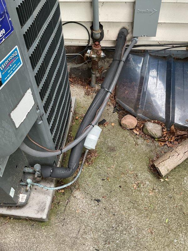 Completed annual cooling maintenance on 17-year-old residential air conditioning system. Performed comprehensive tune-up including inspection of outdoor condenser unit, refrigerant line connections, and associated mechanical components. System found to be in good operating condition with all components functioning within normal parameters. Documented equipment condition with photos showing outdoor installation area, condenser unit with finned coil sections, copper refrigerant lines, brass service valves, and wall-mounted piping connections. Noted typical weathering and aging consistent with outdoor exposure on concrete pad and equipment surfaces. All routine maintenance tasks completed successfully, unit operating properly at time of departure.