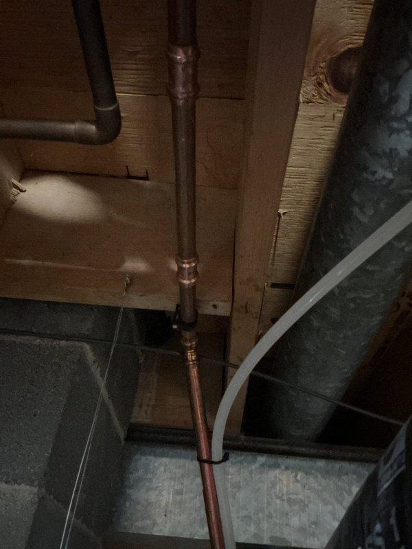 Installed domestic hot water expansion tank on existing water heater system in basement utility area. Mounted blue expansion tank to top of water heater using proper metal clamps and connected to system via copper piping with brass fittings to protect against thermal expansion and maintain system pressure compliance.