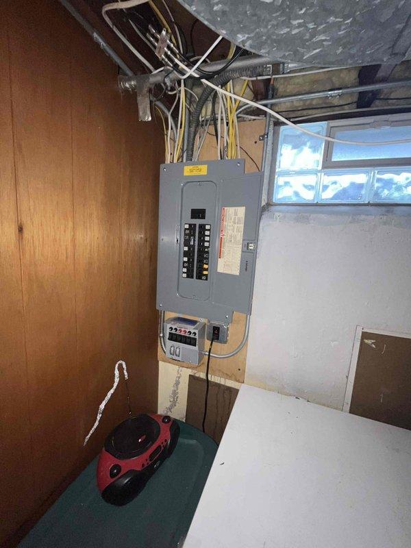 Conducted on-site assessment for new generator installation at approximately 50-year-old residential property. Evaluated existing electrical infrastructure in basement utility area, including main electrical panel with exposed circuit breakers and current metering equipment. Documented electrical service configuration, panel capacity, and available space for transfer switch installation. Photographed existing electrical system layout, wiring routing from panel through ceiling joists, and proximity to ductwork and structural components to determine optimal generator placement and connection points for estimate preparation.
