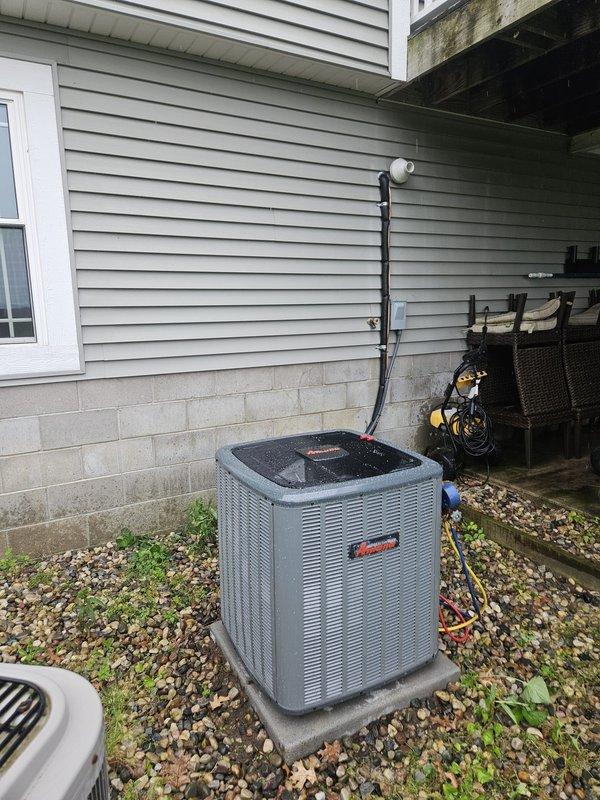 Completed full air conditioning system replacement with installation of new Amana condenser unit on exterior concrete pad with gravel base. Ran refrigerant lines vertically along exterior siding, established all electrical connections, and secured service lines to unit. System was installed against foundation with proper clearances, all connections tested and verified operational.