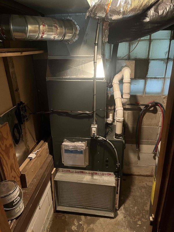 Completed add-on air conditioning installation to existing forced-air heating system in basement mechanical room. Installed evaporator coil unit integrated with existing furnace, including new refrigerant lines and condensate drainage system with white PVC piping configured in proper trap arrangement. Ran metallic flex ductwork from new cooling equipment, connecting to existing trunk line with reflective insulation wrapping. Mounted humidifier unit on furnace cabinet and verified all electrical connections for new AC components. System tested for proper airflow, refrigerant charge, and condensate removal. All equipment operational and ready for cooling season.