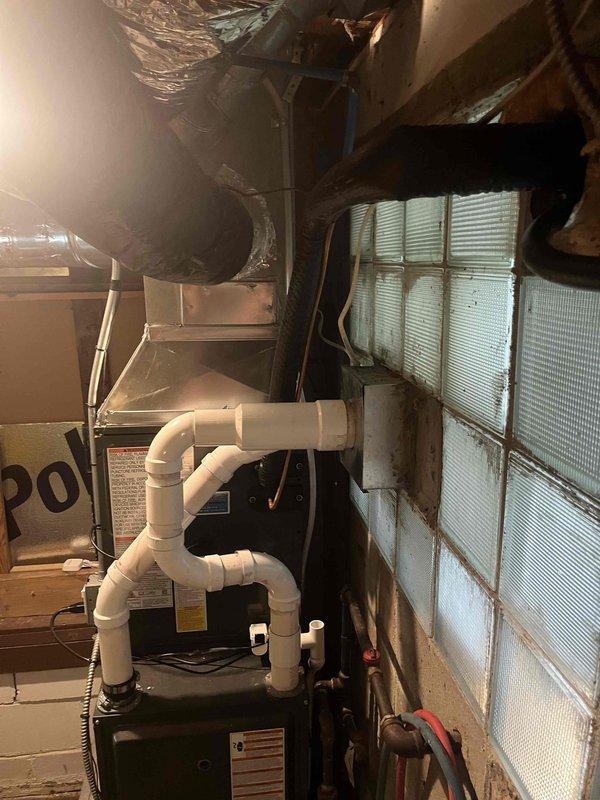 Completed add-on air conditioning installation to existing forced-air heating system in basement mechanical room. Installed evaporator coil unit integrated with existing furnace, including new refrigerant lines and condensate drainage system with white PVC piping configured in proper trap arrangement. Ran metallic flex ductwork from new cooling equipment, connecting to existing trunk line with reflective insulation wrapping. Mounted humidifier unit on furnace cabinet and verified all electrical connections for new AC components. System tested for proper airflow, refrigerant charge, and condensate removal. All equipment operational and ready for cooling season.