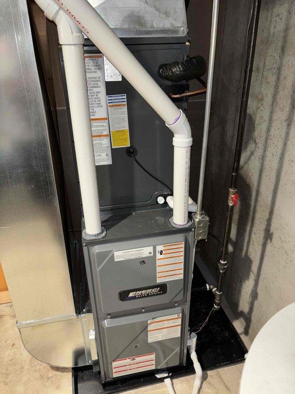Completed full installation of new furnace and air conditioning system in basement utility area. Installed gray metal furnace unit with proper venting using white PVC piping routed upward and connected to insulated ductwork system. Configured refrigerant lines with appropriate valving, secured black piping to concrete wall with mounting brackets, and positioned equipment on protective base pad within mechanical closet. All components installed per manufacturer specifications with proper clearances, connections verified, and system tested for operational readiness.