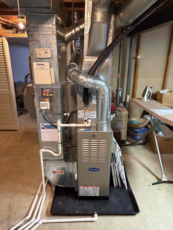 Completed full installation of Carrier brand furnace and air conditioning system in basement utility area. Unit was properly positioned on protective mat, all supply and return ductwork connected including metallic rigid ducts and flexible connections, PVC condensate drainage lines installed and routed appropriately, and new air filter installed in furnace cabinet. System installation verified with all components properly secured and operational.