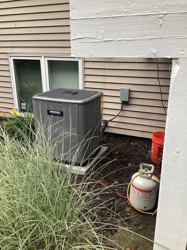 Successfully completed full air conditioning system replacement at residential property. Removed existing outdoor condensing unit and installed new HVAC condenser on concrete pad adjacent to exterior wall with white siding. Ran new refrigerant lines from unit to structure, secured electrical conduit and wiring to exterior wall, and installed disconnect box per code requirements. Unit positioned in landscaped side yard area with proper clearances maintained. All electrical connections completed, system tested, and verified operational. Installation includes proper labeling and safety documentation affixed to equipment.