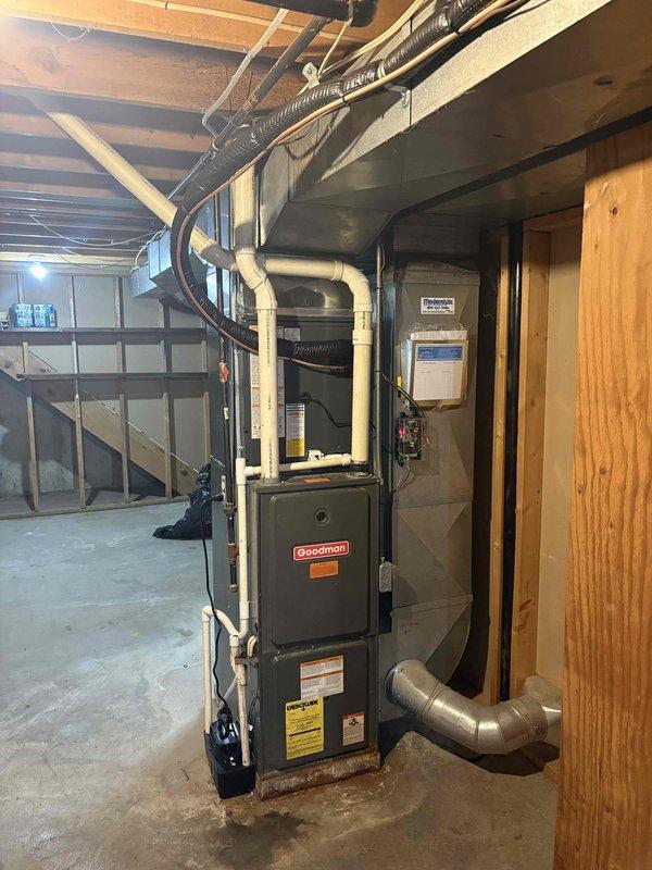 Completed full HVAC system replacement in basement utility area. Removed existing equipment and installed new Goodman brand furnace with matching air handler unit. Ran and secured all necessary ductwork including flexible silver ducting with proper metal strapping. Installed white PVC condensate drain lines with vertical routing for proper drainage. Connected copper refrigerant lines with brass service valves featuring red-handled shut-off ports for system maintenance access. Mounted and wired electrical control panel to wall per code requirements. Verified all connections, tested system operation, and confirmed proper airflow through supply and return ductwork. Installation completed with professional routing of all piping and ductwork through ceiling joists. System tested and left in full operational condition.