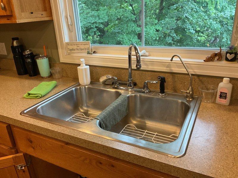 # Drain Diagnostic Service

Responded to customer complaint of gurgling sounds in kitchen sink drain occurring when adjacent laundry room was in use. Upon arrival, inspected both the kitchen sink plumbing and laundry room connections to identify the source of the drainage issue. Examined the double-basin stainless steel kitchen sink and verified the symptom description. Inspected laundry room utility connections including water supply valves and drain lines. 

Diagnosed the gurgling as a venting issue caused by inadequate air circulation in the drain waste vent (DWV) system, which creates negative pressure when the laundry drains, pulling air through the kitchen sink trap. Explained findings to customer and provided recommendations for resolving the venting deficiency. Documented conditions with photographs of both the kitchen sink area and laundry room plumbing connections for reference.