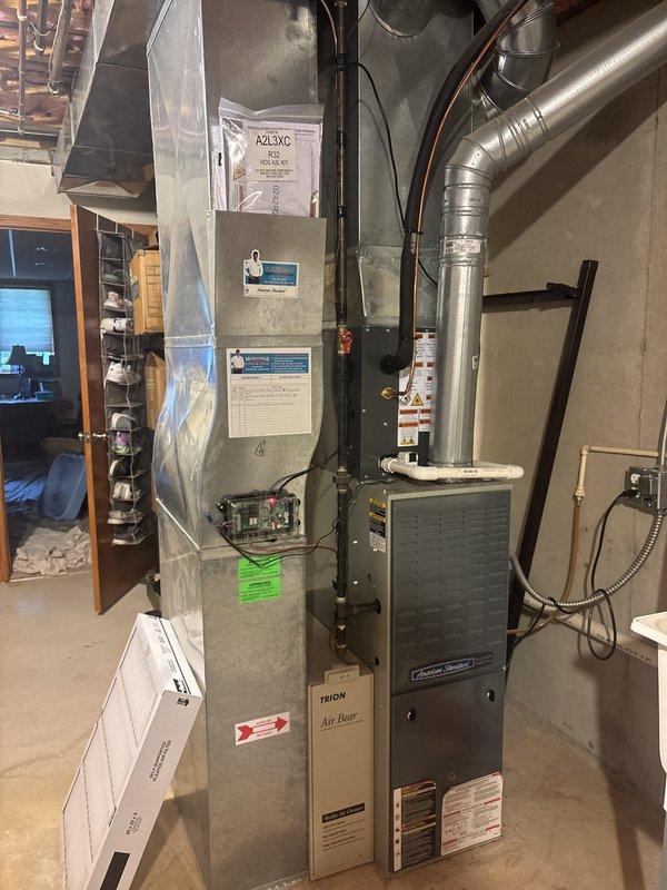 Completed full air conditioning system replacement at residential property. Removed existing outdoor condensing unit and installed new gray outdoor HVAC condenser on concrete pad with proper clearances and landscaping considerations. Indoor installation included new American Standard air handler unit positioned above existing furnace in basement utility area. Established refrigerant line connections using copper lines with proper insulation, secured all ductwork transitions with metallic flex duct, and verified electrical conduit connections to exterior unit. System startup performed with operational checks confirming proper airflow, refrigerant charge, and equipment function across all components.