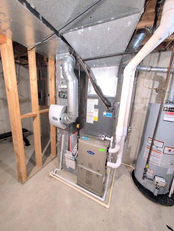 Completed full air conditioning system replacement at residential property. Removed existing outdoor condenser unit and installed new dual-zone HVAC condenser system on concrete pad against exterior wall with proper electrical connections and refrigerant line routing. Installed new indoor air handler unit in basement mechanical room, integrated with existing furnace system. Connected flexible and rigid ductwork throughout basement ceiling space, ensuring proper airflow distribution. Installed and configured white PVC condensate drainage lines from air handler to existing plumbing system. Mounted and wired humidifier unit to HVAC system for climate control integration. Verified all electrical connections, refrigerant charge levels, and system pressures meet manufacturer specifications. Tested complete system operation including cooling cycles, thermostat response, and airflow measurements at all registers. All equipment secured, labeled, and operational per industry standards.