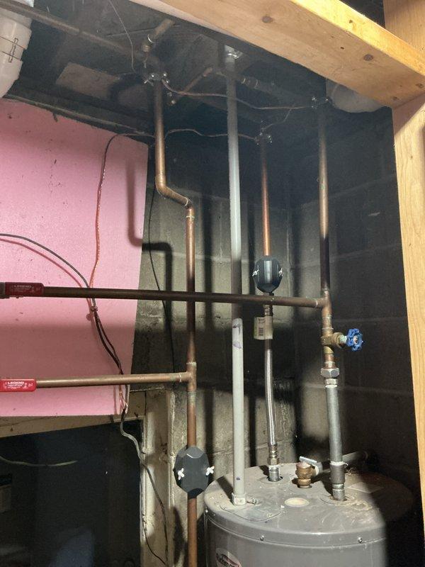 Provided estimate for water heater replacement in unfinished basement utility area. Assessed existing residential water heater installation with copper piping configuration, shutoff valves, and connections to electrical panel. Evaluated surrounding conditions including exposed wooden framing with evidence of previous water damage or staining, electrical panel with circuit breakers, conduit routing, and plumbing infrastructure to determine scope of replacement work and necessary modifications to bring installation up to current code requirements.