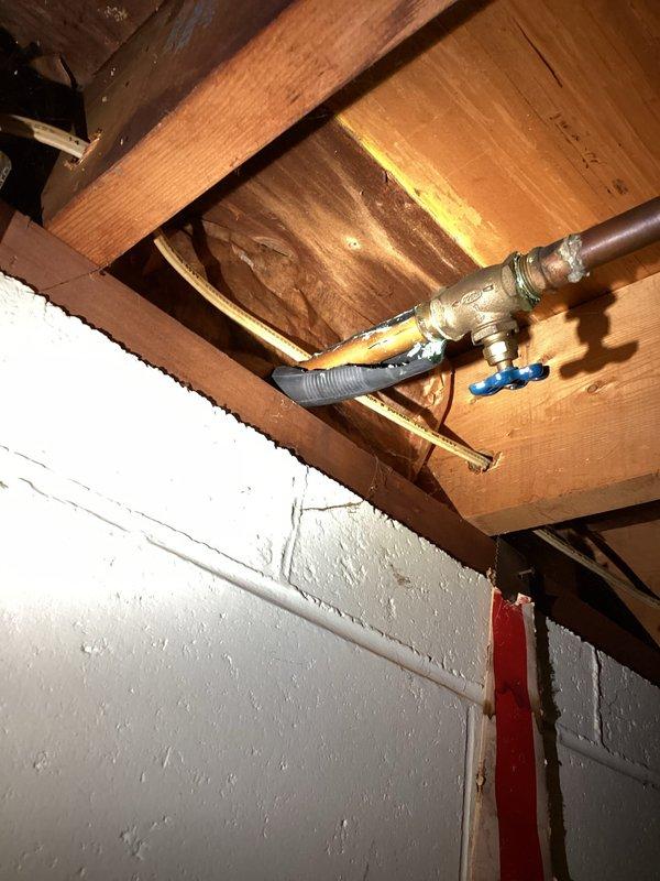 Responded to plumbing leak complaint involving outdoor hose spigot leaking into interior of home. Upon inspection, identified compromised outdoor spigot assembly causing water infiltration through exterior wall into basement area. Observed water damage evidence on exterior concrete foundation with moisture accumulation near building perimeter. Interior inspection revealed plumbing connections at ceiling joists with brass T-junction fitting and shutoff valve in basement utility area. Repaired leaking outdoor spigot assembly to eliminate water intrusion into structure. Verified proper operation of shutoff valve and plumbing connections. Resolved leak issue preventing further water damage to interior and foundation areas.