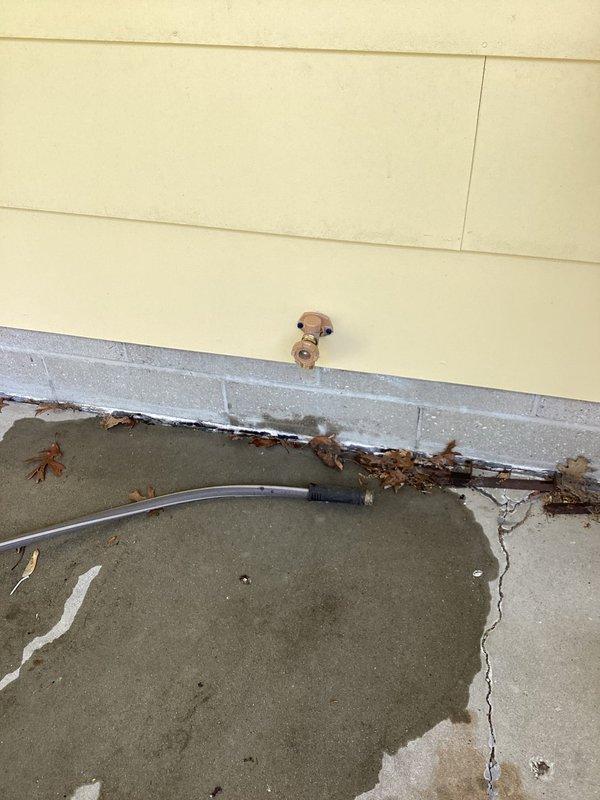 Responded to plumbing leak complaint involving outdoor hose spigot leaking into interior of home. Upon inspection, identified compromised outdoor spigot assembly causing water infiltration through exterior wall into basement area. Observed water damage evidence on exterior concrete foundation with moisture accumulation near building perimeter. Interior inspection revealed plumbing connections at ceiling joists with brass T-junction fitting and shutoff valve in basement utility area. Repaired leaking outdoor spigot assembly to eliminate water intrusion into structure. Verified proper operation of shutoff valve and plumbing connections. Resolved leak issue preventing further water damage to interior and foundation areas.