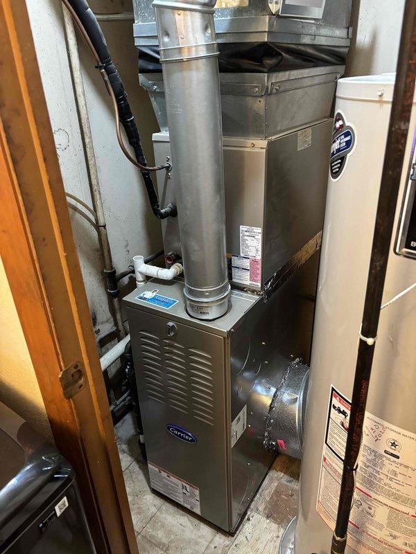 Completed full furnace installation in residential utility closet. Installed new Carrier-brand furnace unit with proper clearances for maintenance access. Connected vertical flue piping and integrated ductwork to existing HVAC system. Secured all mounting brackets and verified proper ventilation. Installation includes complete connection of supply and return air systems with black metal ductwork routing. All manufacturer specifications followed for equipment placement adjacent to existing water heater. System installed on concrete pad with appropriate spacing per code requirements.