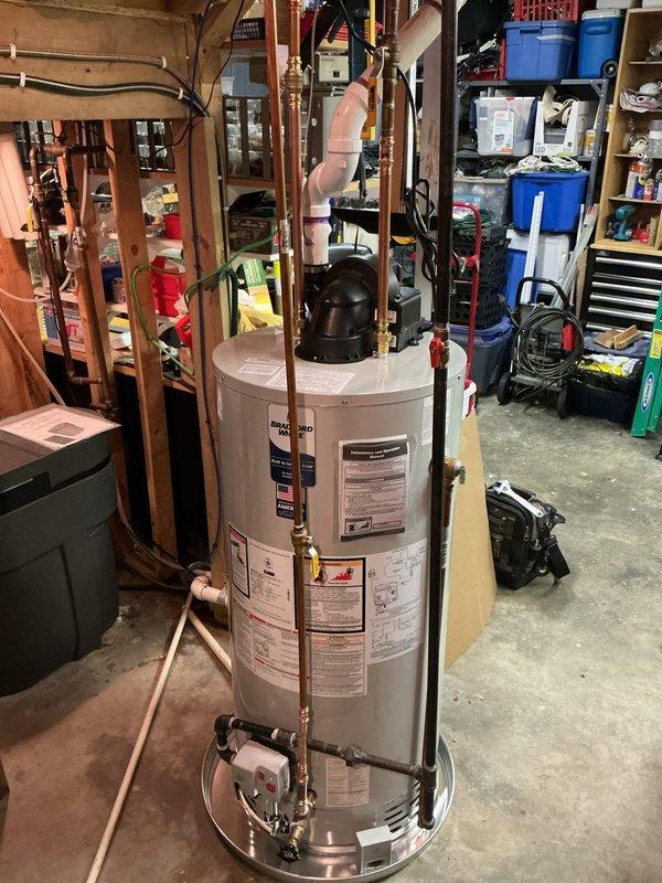 Completed installation of 50-gallon natural gas water heater in basement utility area. Unit was properly positioned on concrete floor with drain pan, connected copper supply lines with brass fittings to inlet and outlet ports, installed black expansion tank on top of unit, and verified all plumbing connections were secure and leak-free. All manufacturer specifications, safety labels, and code requirements were confirmed during installation.
