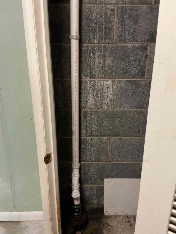 Completed kitchen stack and main drain stack replacement in basement utility area. Removed deteriorated cast iron drainage piping and installed new white PVC drainage system with proper fittings, couplings, and mounting brackets secured to concrete block wall. New drain line extends vertically from floor connection through ceiling to service upper-level kitchen fixtures, with black rubber boot coupling at floor penetration point ensuring watertight seal at base connection.