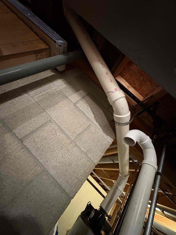 Provided water heater replacement estimate for 25-year-old unit located in basement utility area. Inspected existing white cylindrical water heater on raised concrete platform with copper and PVC connections, including white PVC exhaust vent and gas lines. Documented current installation configuration including proximity to blue water softener system and furnace unit, assessed routing of supply and exhaust piping through ceiling space to upper levels, and photographed all relevant mechanical connections for replacement planning.