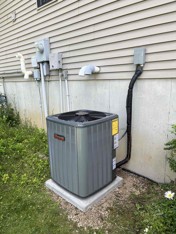 Completed full residential HVAC system installation including furnace and air conditioning unit. Installed dark-colored vertical furnace in utility closet with complete PVC venting and drainage network, including multiple vertical and angled pipe configurations for proper exhaust and condensate management. Mounted outdoor condensing unit on concrete pad with proper electrical disconnect, conduit routing, and refrigerant line connections to house exterior. All manufacturer labels, safety compliance stickers, and energy guide documentation properly affixed to equipment. System installed per manufacturer specifications with secure mounting, proper clearances, and complete electrical connections verified.