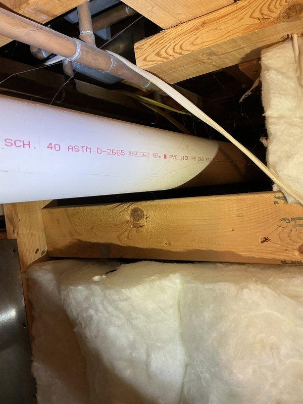 Responded to emergency call for 20-year-old water heater that had failed and was actively leaking, causing flooding in the utility area. Upon arrival, assessed the unit and confirmed complete failure due to age-related deterioration. Shut off water supply to prevent further flooding, drained the failed unit, and documented the installation location in the attic/crawl space area with existing HVAC ductwork and PVC plumbing infrastructure. Photographed the work area showing the white cylindrical water heater, surrounding wooden beam structure, insulation, and connected piping systems for service records.