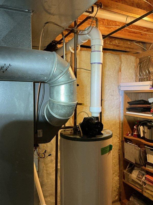 Responded to emergency call for 20-year-old water heater that had failed and was actively leaking, causing flooding in the utility area. Upon arrival, assessed the unit and confirmed complete failure due to age-related deterioration. Shut off water supply to prevent further flooding, drained the failed unit, and documented the installation location in the attic/crawl space area with existing HVAC ductwork and PVC plumbing infrastructure. Photographed the work area showing the white cylindrical water heater, surrounding wooden beam structure, insulation, and connected piping systems for service records.
