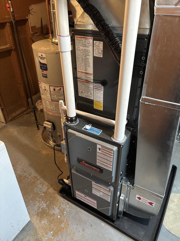 Completed full installation of residential HVAC system and water heater in basement utility area. Installed gray metal dual-compartment furnace unit with proper venting using white PVC exhaust pipes on both sides and black flexible ductwork connection at top. Mounted and connected silver metallic air conditioning components adjacent to furnace. Installed white cylindrical water heater with metallic vertical vent pipe, brass fittings, and proper copper and PVC piping connections. All equipment positioned on concrete floor with appropriate clearances, manufacturer specification labels visible and accessible, and venting systems properly terminated. Michigan Saves financing documentation processed and submitted through DocuSign for project approval. System installation completed per manufacturer specifications with all safety requirements met and equipment operational.