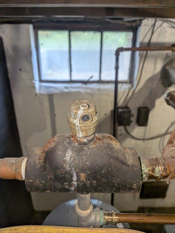 Completed comprehensive boiler tune-up on aging heating system with visible corrosion on manifold assembly and copper piping connections. Performed standard maintenance procedures including inspection of black rectangular manifold unit, circulator pump motor, U-bend copper piping, and all electrical connections; system operational upon completion despite advanced age and surface oxidation on components.