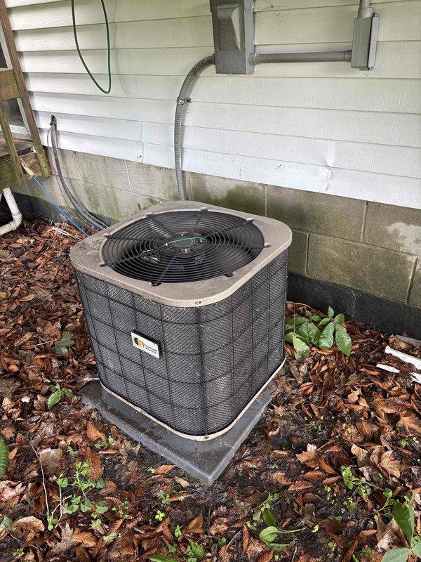 Completed annual cooling maintenance on a 25-year-old Thermal Zone air conditioning system. Performed comprehensive tune-up of outdoor condenser unit, including inspection of cylindrical housing, protective wire mesh grille, and fan assembly. Verified proper electrical connections at junction box and conduit routing. Assessed unit operation and airflow through top-mounted fan. Documented equipment condition with photos showing unit positioned on concrete pad with adequate clearance, though surrounding area exhibits vegetation growth and debris accumulation in mulch bed that may benefit from future cleaning to maintain optimal airflow and prevent potential blockages.