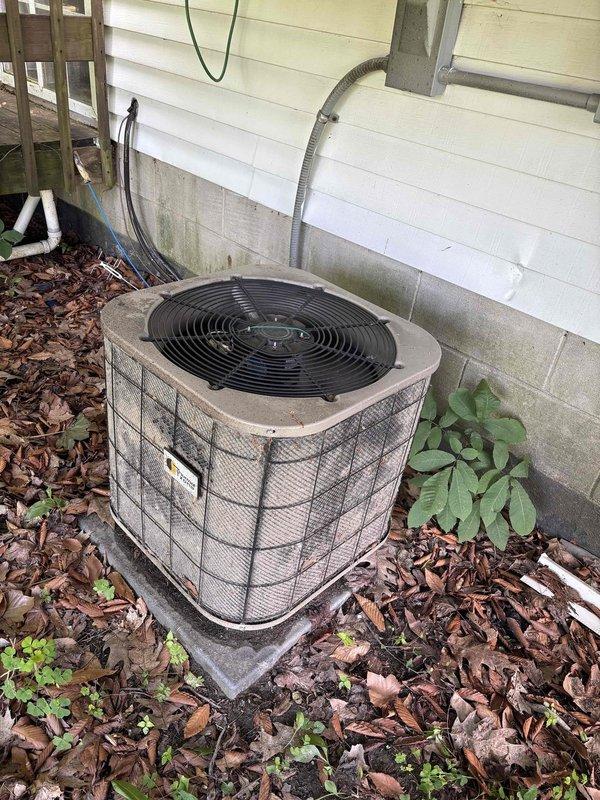 Completed annual cooling maintenance on a 25-year-old Thermal Zone air conditioning system. Performed comprehensive tune-up of outdoor condenser unit, including inspection of cylindrical housing, protective wire mesh grille, and fan assembly. Verified proper electrical connections at junction box and conduit routing. Assessed unit operation and airflow through top-mounted fan. Documented equipment condition with photos showing unit positioned on concrete pad with adequate clearance, though surrounding area exhibits vegetation growth and debris accumulation in mulch bed that may benefit from future cleaning to maintain optimal airflow and prevent potential blockages.