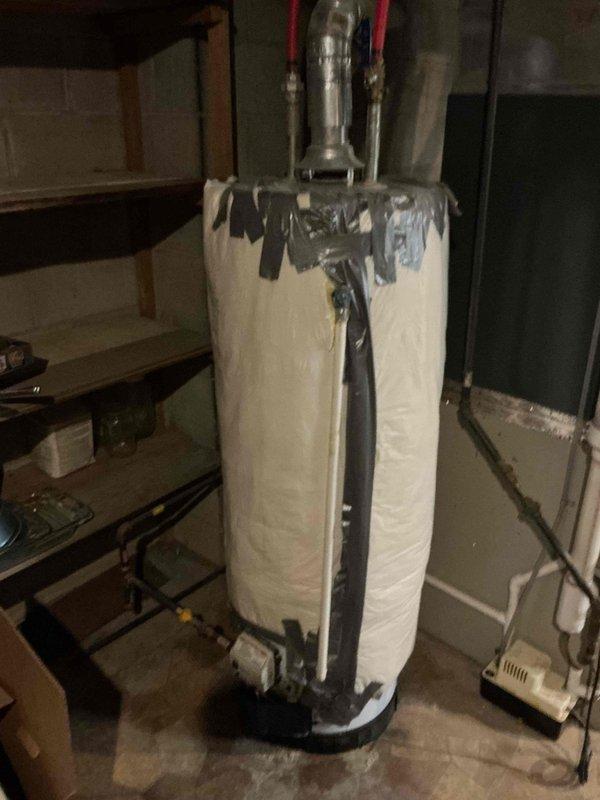 Responded to residential plumbing leak in basement utility area involving water heater discharge. Upon arrival, identified active dripping from temperature and pressure relief (TPR) valve discharge pipe onto concrete floor. Inspected water heater installation, noting unit wrapped in reflective insulation blanket with red-handled shutoff valves and various copper and PVC connections at top of tank. Examined TPR valve operation and discharge piping configuration to determine source of leak. Documented equipment condition and leak location with photographs showing water heater positioned in drain pan, adjacent furnace system, and overhead ductwork. Assessed floor area for water damage and verified proper drainage. Completed leak diagnosis and provided recommendations for necessary repairs to eliminate water discharge issue.