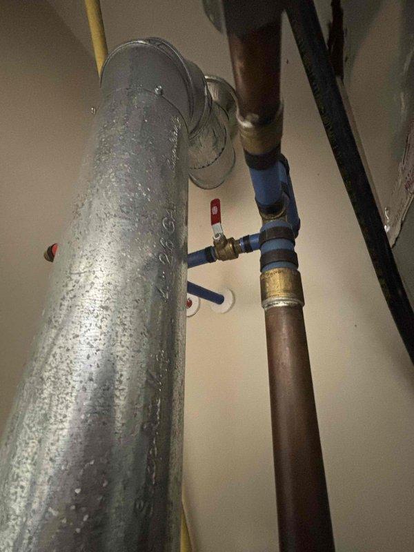 Responded to service call for water heater leaking from bottom. Upon inspection, observed heavy condensation on cylindrical metal piping and connections in mechanical room, with water heater showing signs of base leakage. Documented existing plumbing configuration including copper supply lines with shutoff valves, oxidized copper piping, and connections to HVAC system components. Photographed affected equipment and surrounding area including Carrier furnace installation and PVC venting system. Provided estimate for water heater replacement due to bottom leak condition, which typically indicates internal tank failure requiring full unit replacement rather than repair.