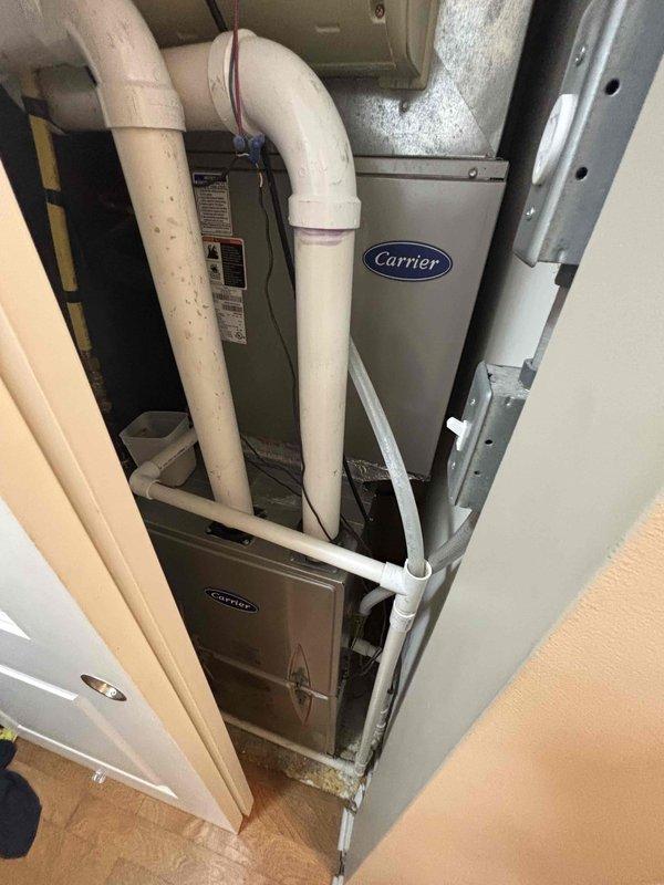 Responded to service call for water heater leaking from bottom. Upon inspection, observed heavy condensation on cylindrical metal piping and connections in mechanical room, with water heater showing signs of base leakage. Documented existing plumbing configuration including copper supply lines with shutoff valves, oxidized copper piping, and connections to HVAC system components. Photographed affected equipment and surrounding area including Carrier furnace installation and PVC venting system. Provided estimate for water heater replacement due to bottom leak condition, which typically indicates internal tank failure requiring full unit replacement rather than repair.