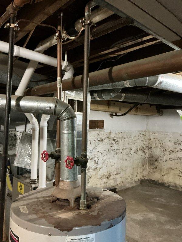 Completed water heater replacement estimate for a 16-year-old residential unit located in basement utility area. Assessed existing water heater configuration including copper supply lines, red-handled shut-off valves, PVC venting, and connection points to building infrastructure. Documented current installation conditions, surrounding plumbing and HVAC systems, and photographed equipment for replacement specifications.
