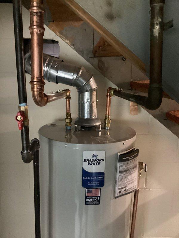 Successfully installed a 40-gallon natural gas Bradford White tall water heater with natural draft venting in basement utility area beneath staircase. Completed all plumbing connections using copper piping with compression fittings and brass components, installed safety valve with pressure relief piping, and verified proper gas line connections to unit. System tested and confirmed operational with no leaks detected.