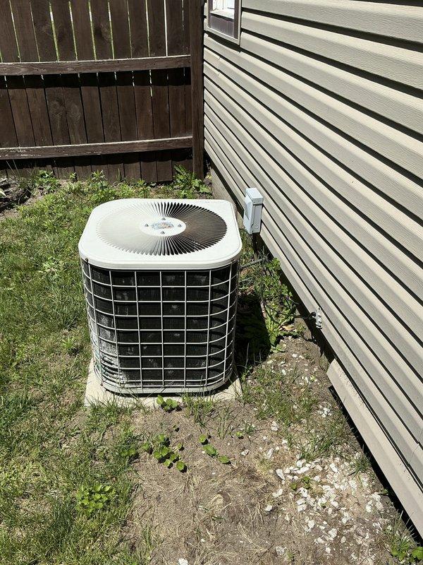 Completed estimate for residential air conditioning system. Inspected outdoor condenser unit positioned on concrete pad between building and privacy fence, documented current equipment condition and installation setup. Photographed unit configuration, electrical disconnect, and surrounding area for estimate preparation.