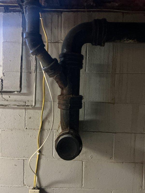 Responded to kitchen drain running slow due to suspected improper venting and incorrect plumbing configuration. Upon inspection, identified horizontal drain line in basement with inadequate pitch and corroded cast iron piping with deteriorated joints contributing to drainage issues. Documented existing plumbing system showing improperly installed drain line secured to floor joists and aging cast iron stack with visible rust and corrosion at connection points affecting flow capacity.