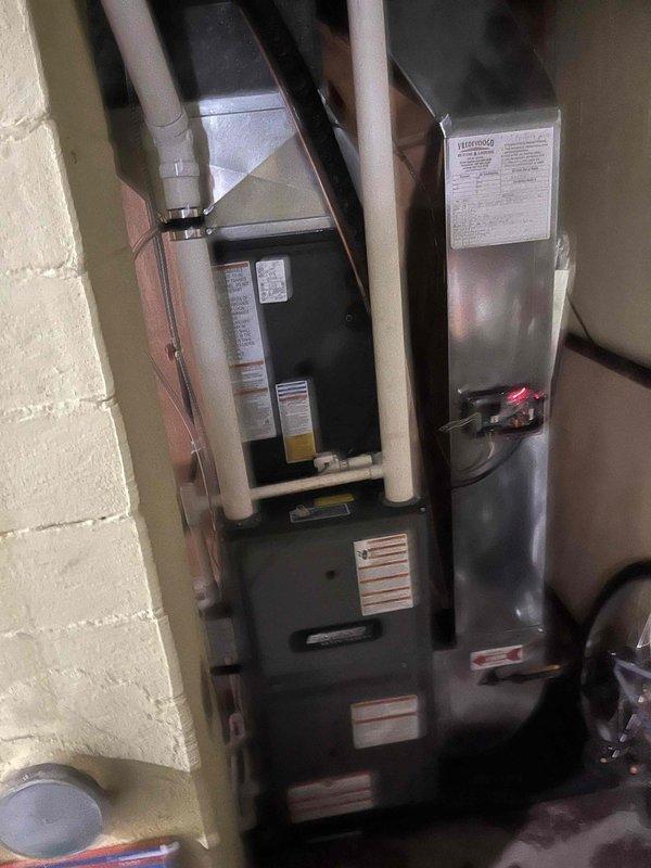 Completed full air conditioning system replacement at residential property. Removed existing HVAC equipment and installed new furnace unit with black metal casing in basement utility room, positioning unit adjacent to existing water heater. Installed all necessary condensate drain lines using white PVC piping with proper vertical routing for drainage. Connected electrical wiring, ductwork components, and support infrastructure to furnace system per manufacturer specifications.

Installed new outdoor condenser unit on existing concrete pad in side yard between structures. Unit features silver-gray casing with horizontal slat design and black protective top grille. Secured condenser to pad and verified proper clearances from adjacent buildings and fence line for adequate airflow and future maintenance access. Connected refrigerant lines between indoor and outdoor units with proper insulation. Completed all electrical connections to condenser unit and verified proper voltage supply.

Test