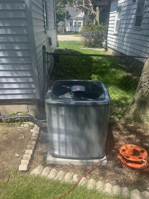 Completed full air conditioning system replacement at residential property. Removed existing HVAC equipment and installed new furnace unit with black metal casing in basement utility room, positioning unit adjacent to existing water heater. Installed all necessary condensate drain lines using white PVC piping with proper vertical routing for drainage. Connected electrical wiring, ductwork components, and support infrastructure to furnace system per manufacturer specifications.

Installed new outdoor condenser unit on existing concrete pad in side yard between structures. Unit features silver-gray casing with horizontal slat design and black protective top grille. Secured condenser to pad and verified proper clearances from adjacent buildings and fence line for adequate airflow and future maintenance access. Connected refrigerant lines between indoor and outdoor units with proper insulation. Completed all electrical connections to condenser unit and verified proper voltage supply.

Test